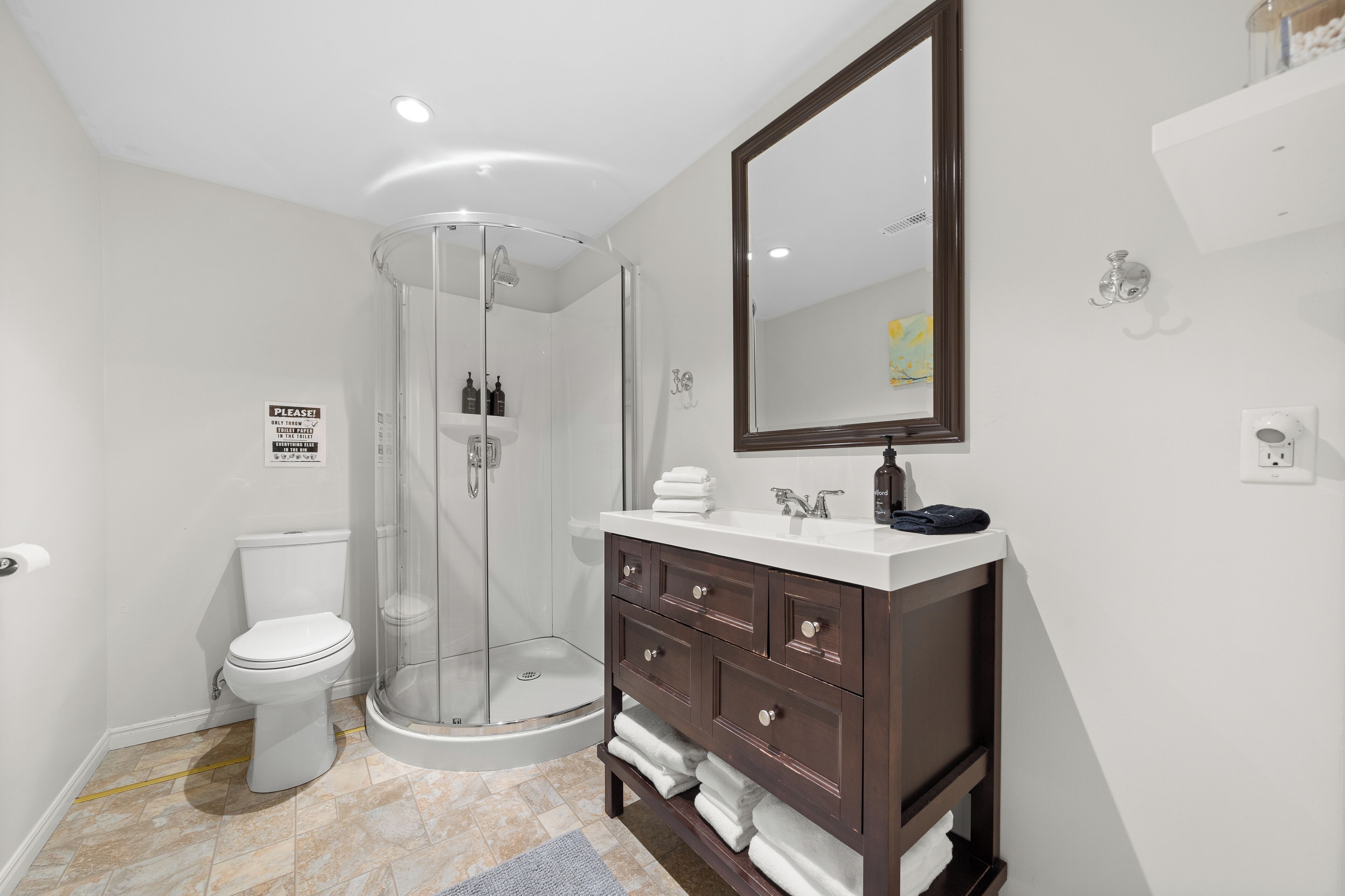 A modern bathroom with a glass-enclosed shower, a white toilet, and a dark wooden vanity with a mirror.