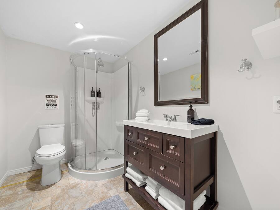 A modern bathroom with a glass-enclosed shower, a white toilet, and a dark wooden vanity with a mirror.