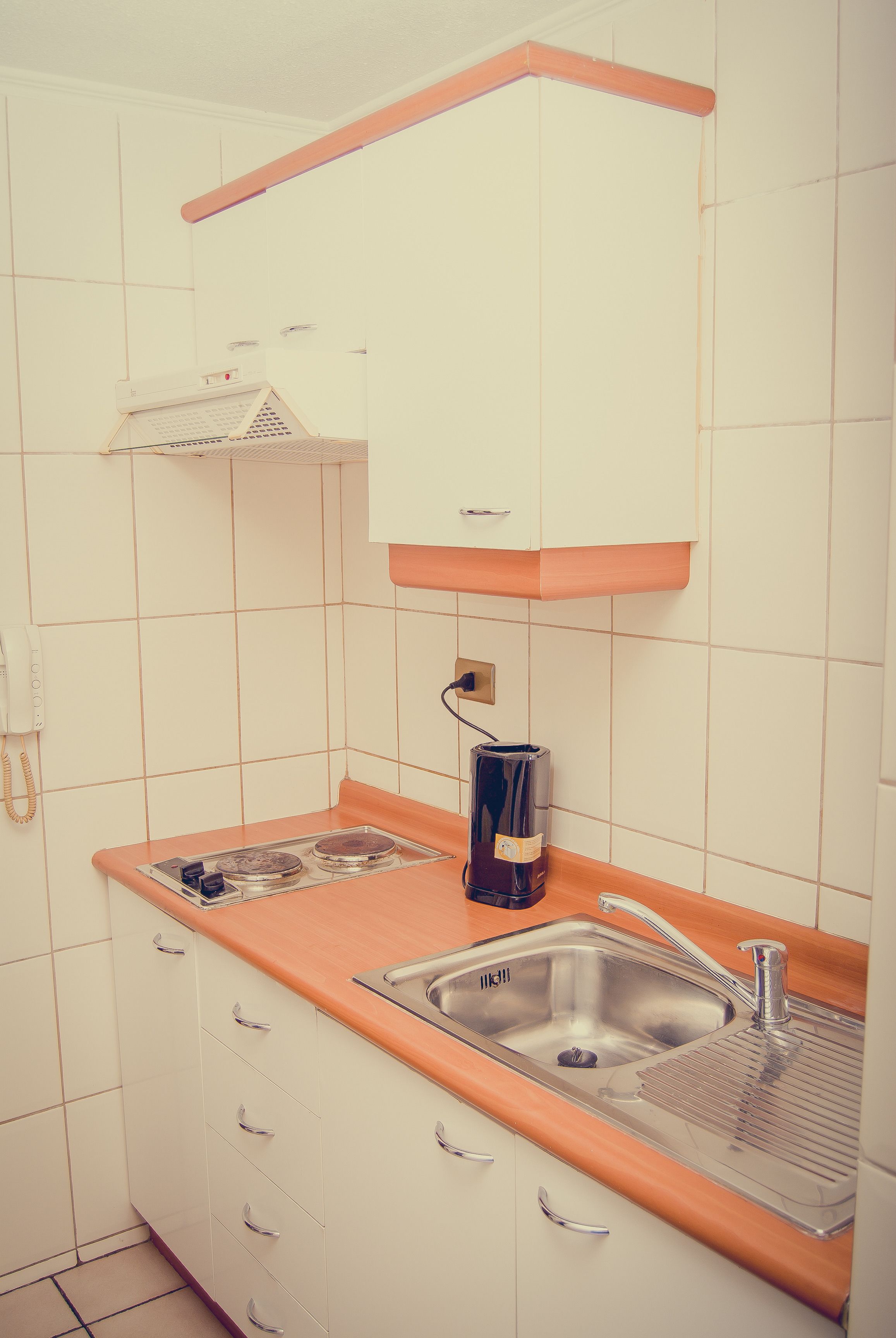 Eine kleine Küche mit weißen Schränken, einer doppelten Spüle und einer Kaffeemaschine.
