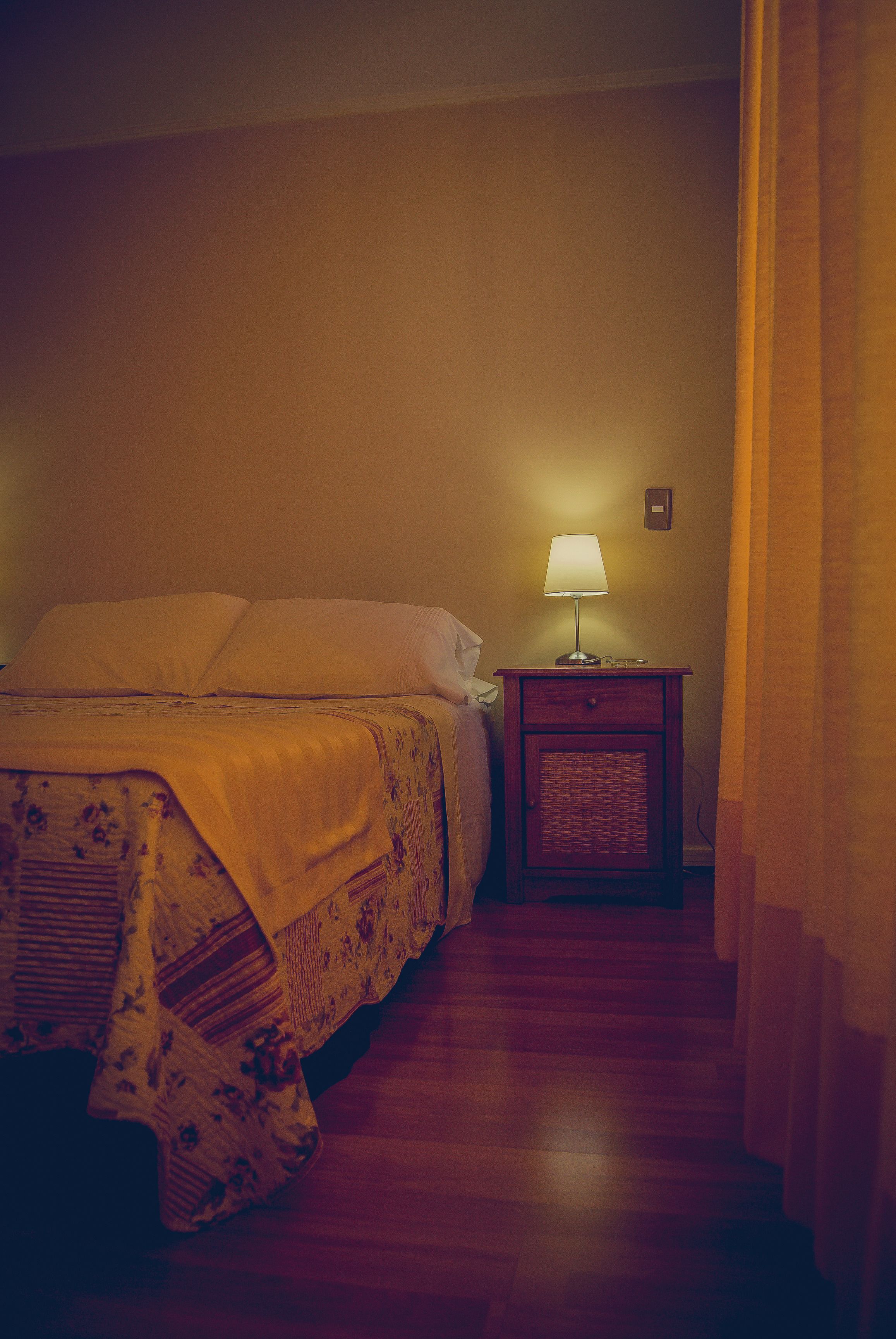 A bedroom with a bed, a nightstand with a lamp, and a wall-mounted light switch.