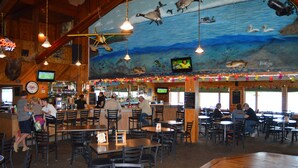 A restaurant with a nautical mural, wooden ceiling beams, and a bar area. - Sportsman's Lodge (Baudette)