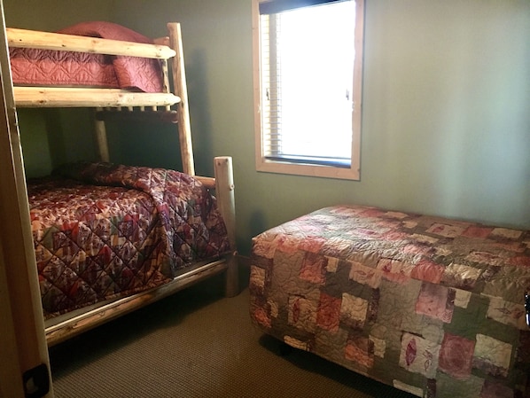 Um quarto com beliches e uma cama de solteiro, uma janela com cortinas e piso coberto de carpete.
