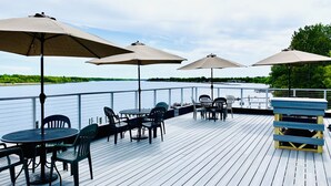 A deck with outdoor seating, including tables and chairs, and large umbrellas. - Sportsman's Lodge (Baudette)