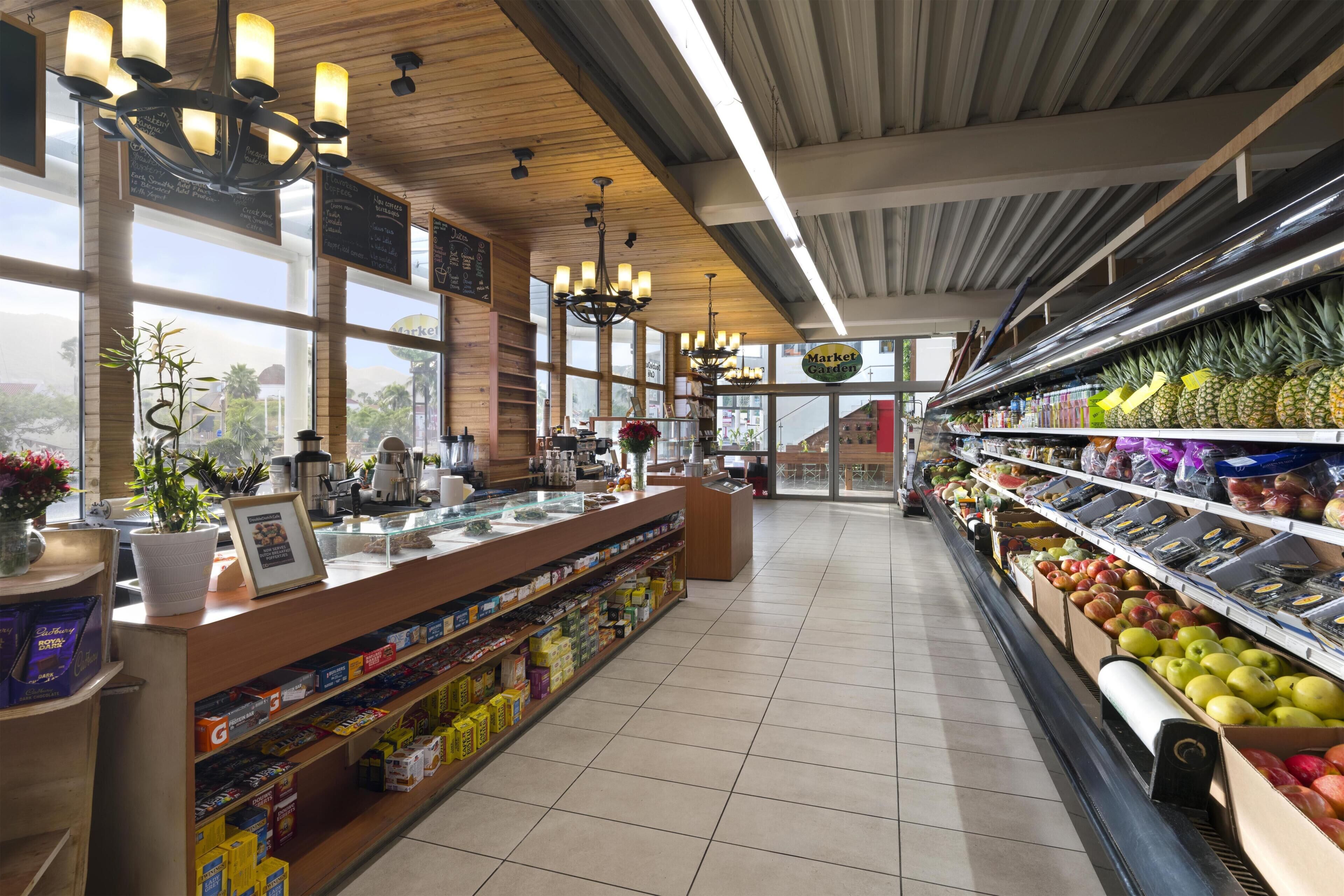 Interior de un supermercado con mostrador de charcutería, vitrina refrigerada y estantes llenos de frutas y productos envasados.