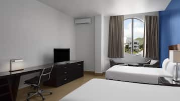 Habitación de hotel con cama, escritorio, silla, televisor y ventana con cortinas.