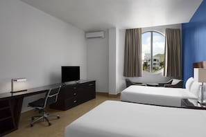 Hotelkamer met een bed, bureau, stoel, televisie en raam met gordijnen.