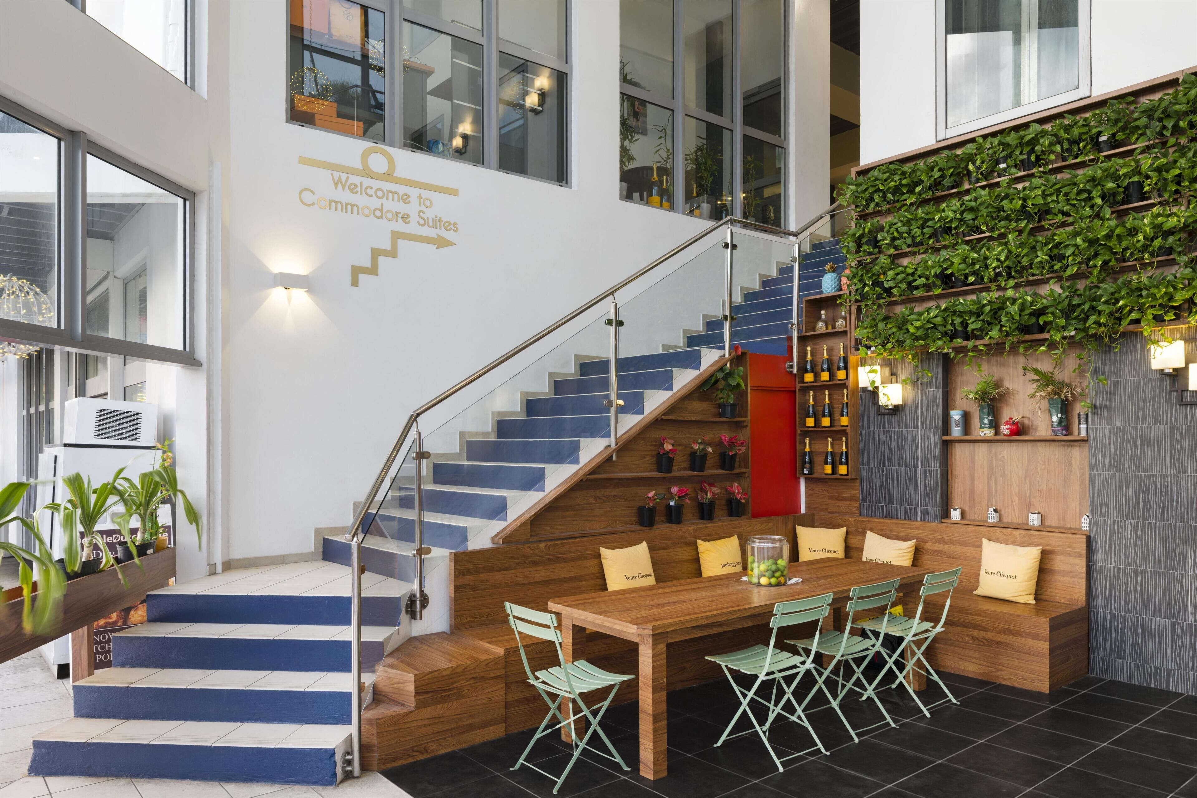 Interior de hotel moderno com escadaria, balcão de recepção e painel de plantas na parede.