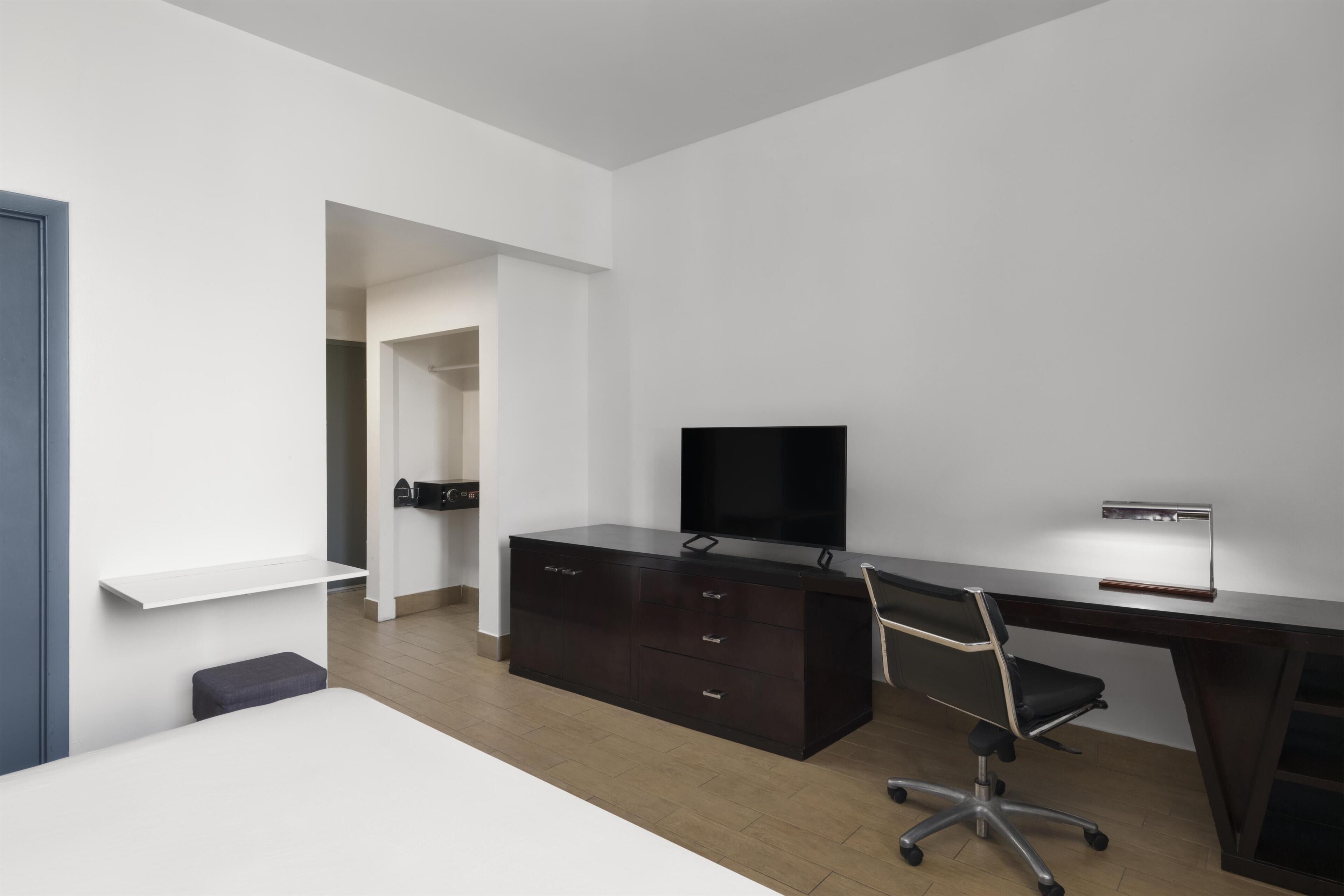 Un dormitorio moderno con cama, escritorio, silla y televisor.