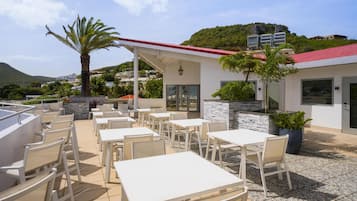 Een terras met witte tafels en stoelen, een stenen muur en uitzicht op een berg.