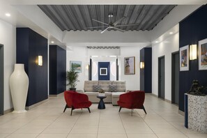 A modern interior with a ceiling fan, a sofa, two red chairs, a coffee table, and artwork on the walls. - Commodore Suites, SureStay Collection by Best Western (Simpson Bay)