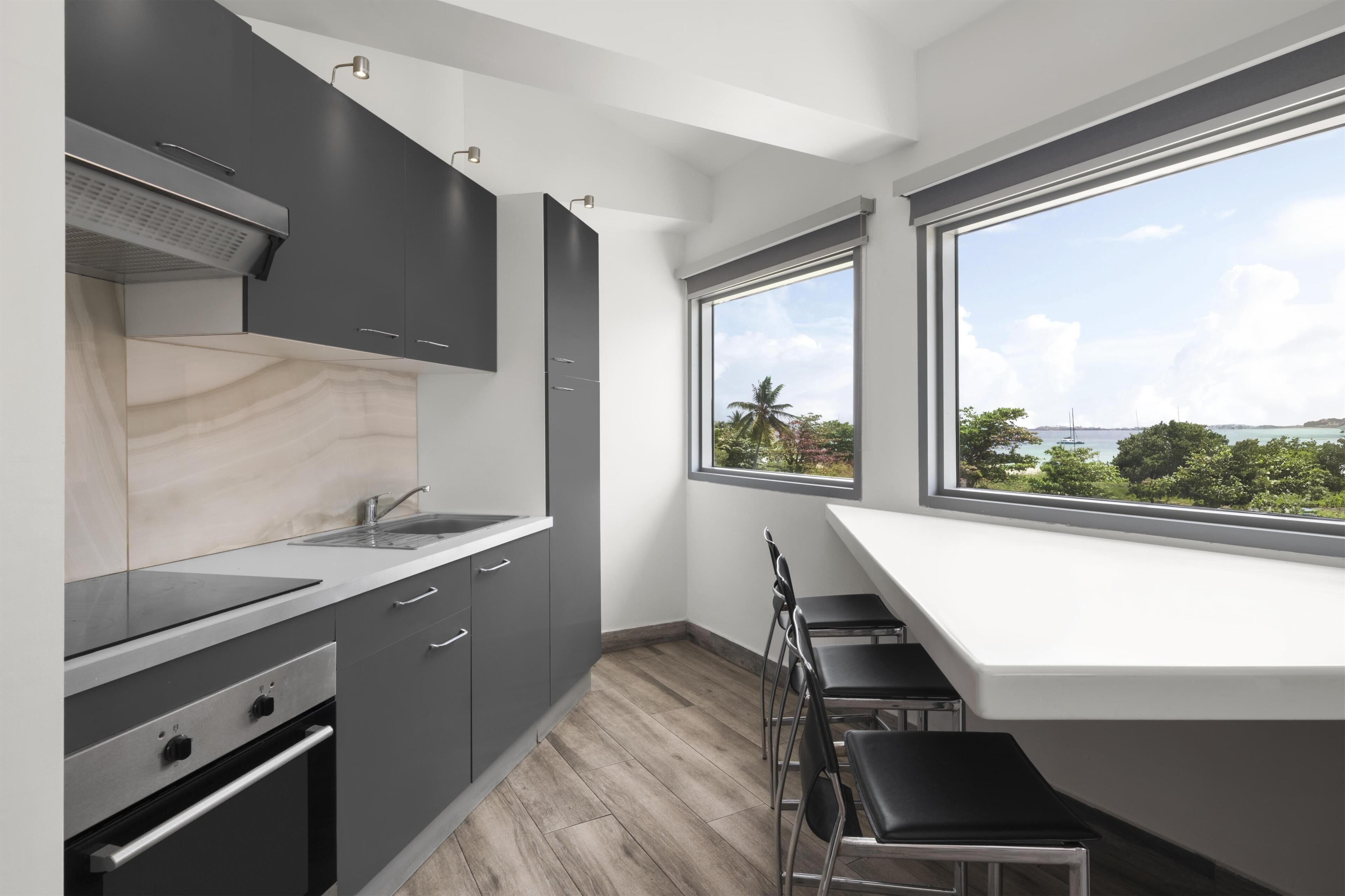 A modern kitchen with a large window, a built-in oven, and a dining area with a view of the sea.