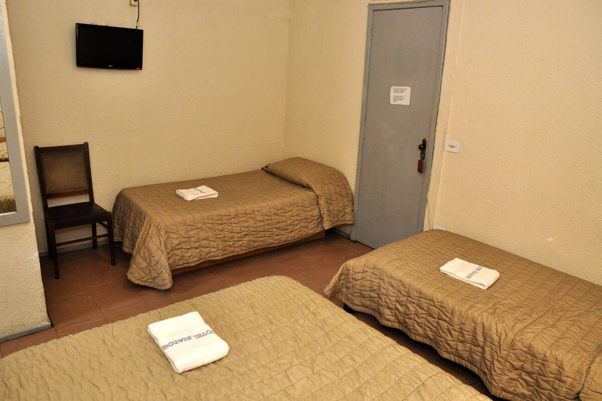 A room with two single beds, a chair, a television mounted on the wall, and a door with a sign.