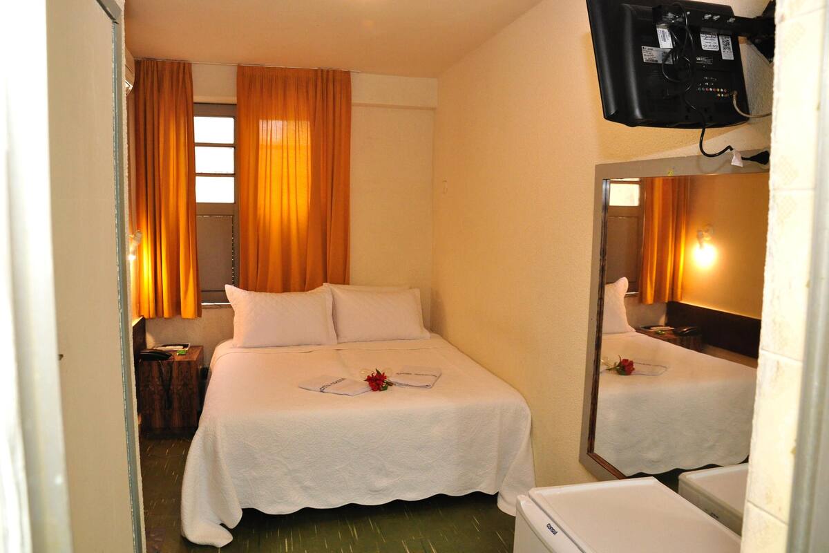 A hotel room with a bed, a bedside table, a mirror, and a television mounted on the wall.