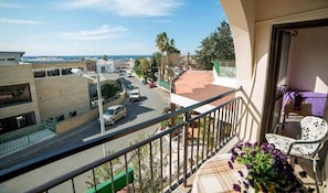 A balcony with a view of a street, a chair, and a potted plant.