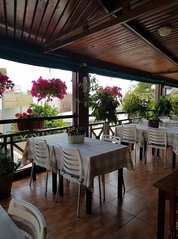 An outdoor patio area with tables and chairs, potted plants, and a view of the cityscape.