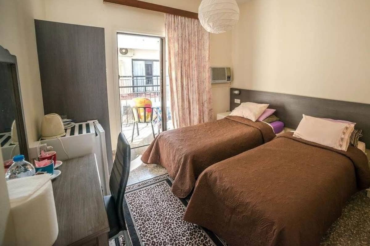 Quarto de hotel com duas camas, uma escrivaninha, uma cadeira, uma mesa e vista para varanda.