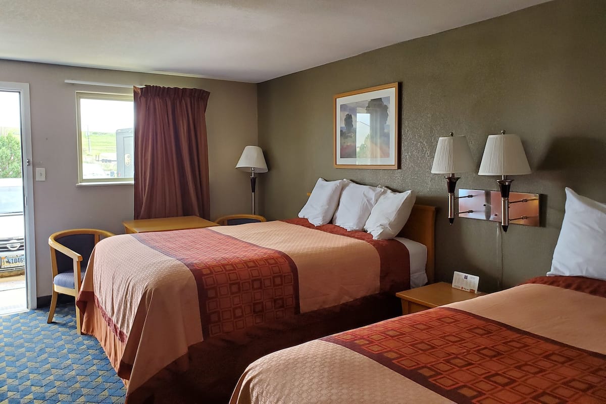 Quarto de hotel com duas camas, uma escrivaninha, uma cadeira e uma janela com vista para o exterior.