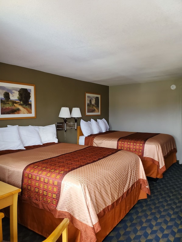 A hotel room with two beds, a desk, two lamps, and two paintings on the wall.