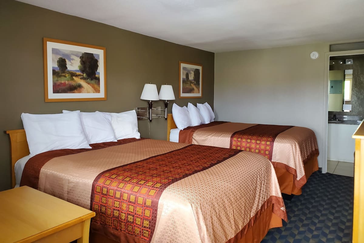 Quarto de hotel com duas camas, uma escrivaninha, uma mesa de cabeceira, duas luminárias fixadas na parede e duas pinturas emolduradas.