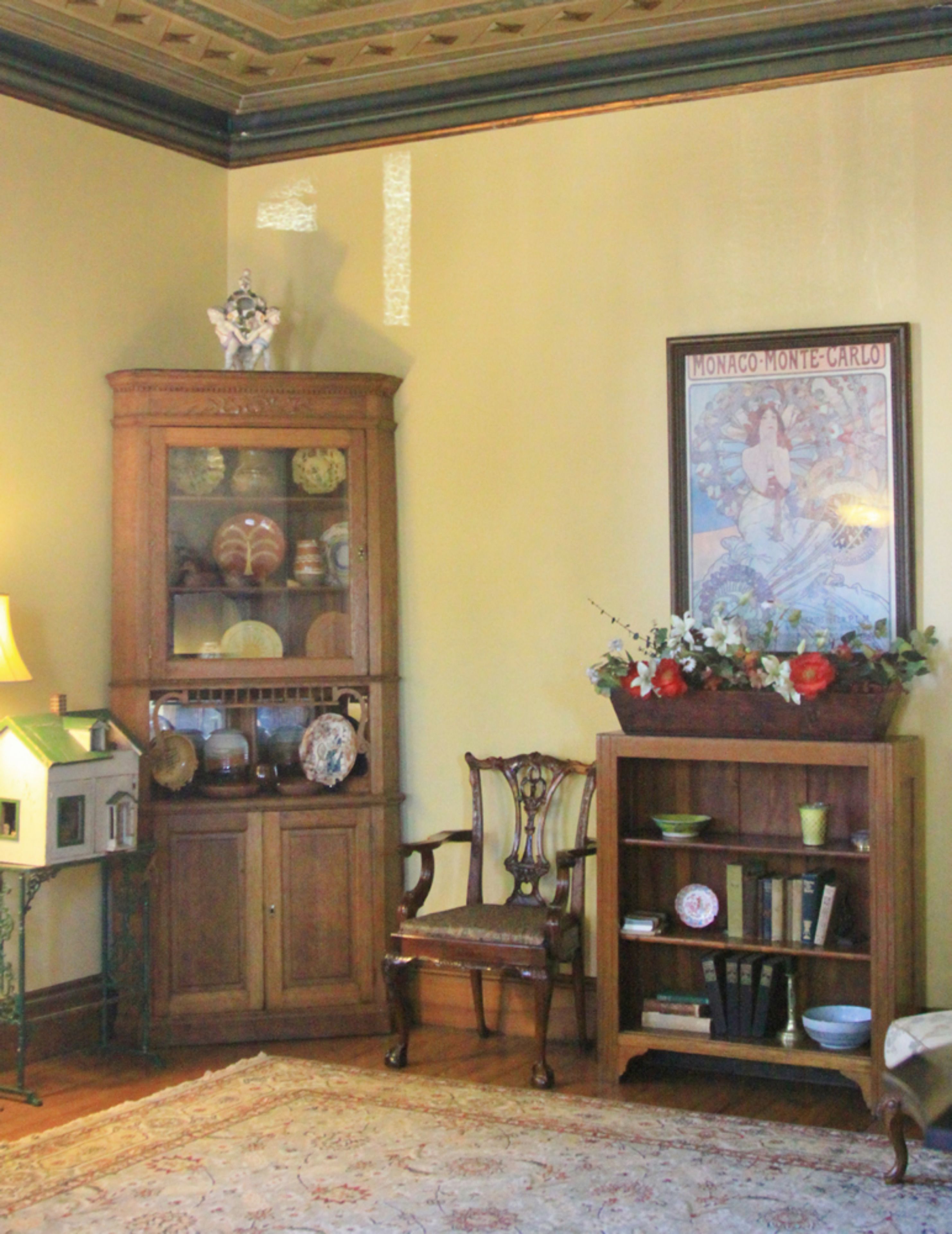 A traditional room with a wooden cabinet, a chair, a bookshelf, and a framed picture on the wall.