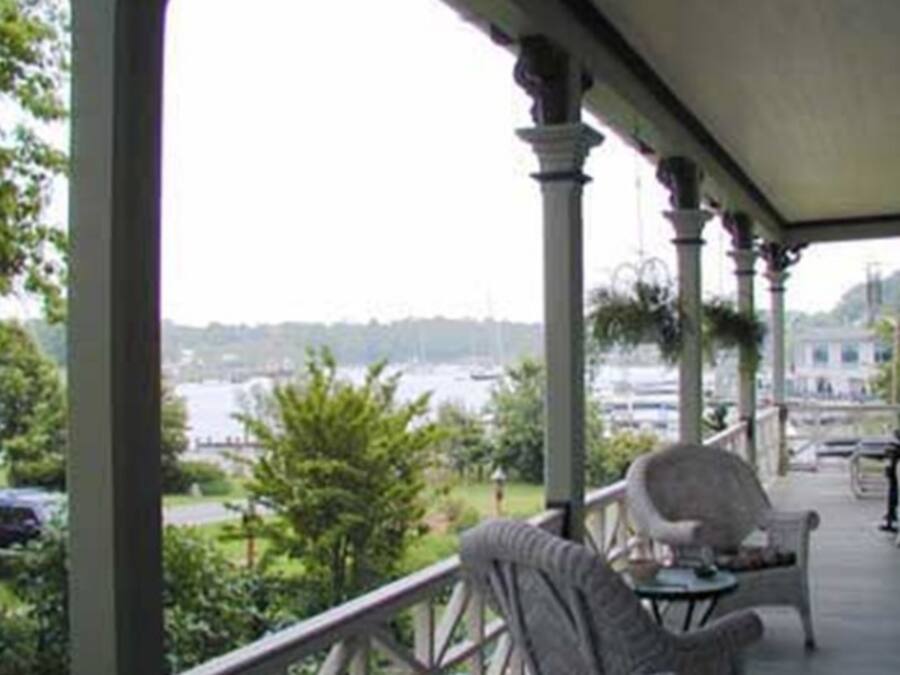 Une véranda couverte, meublée de meubles en osier, donnant sur une marina avec des bateaux et offrant une vue sur l’eau.