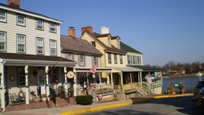 A row of historic buildings with a waterfront view, featuring a porch with American flags and a clock. - Inn At The Canal Bed & Breakfast (Chesapeake City)