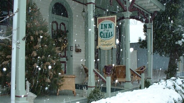 A snow-covered porch with a sign for 'Inn at the Canal' and a Christmas tree. - Inn At The Canal Bed & Breakfast (Chesapeake City)
