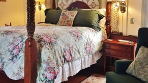 A four-poster bed with floral bedding, a green armchair, and a patterned wall hanging. - Inn At The Canal Bed & Breakfast (Chesapeake City)
