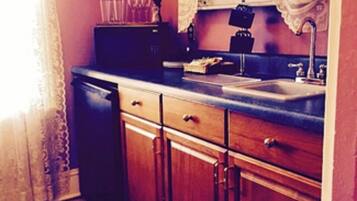 A kitchen with wooden cabinets, a sink, and a window with lace curtains.