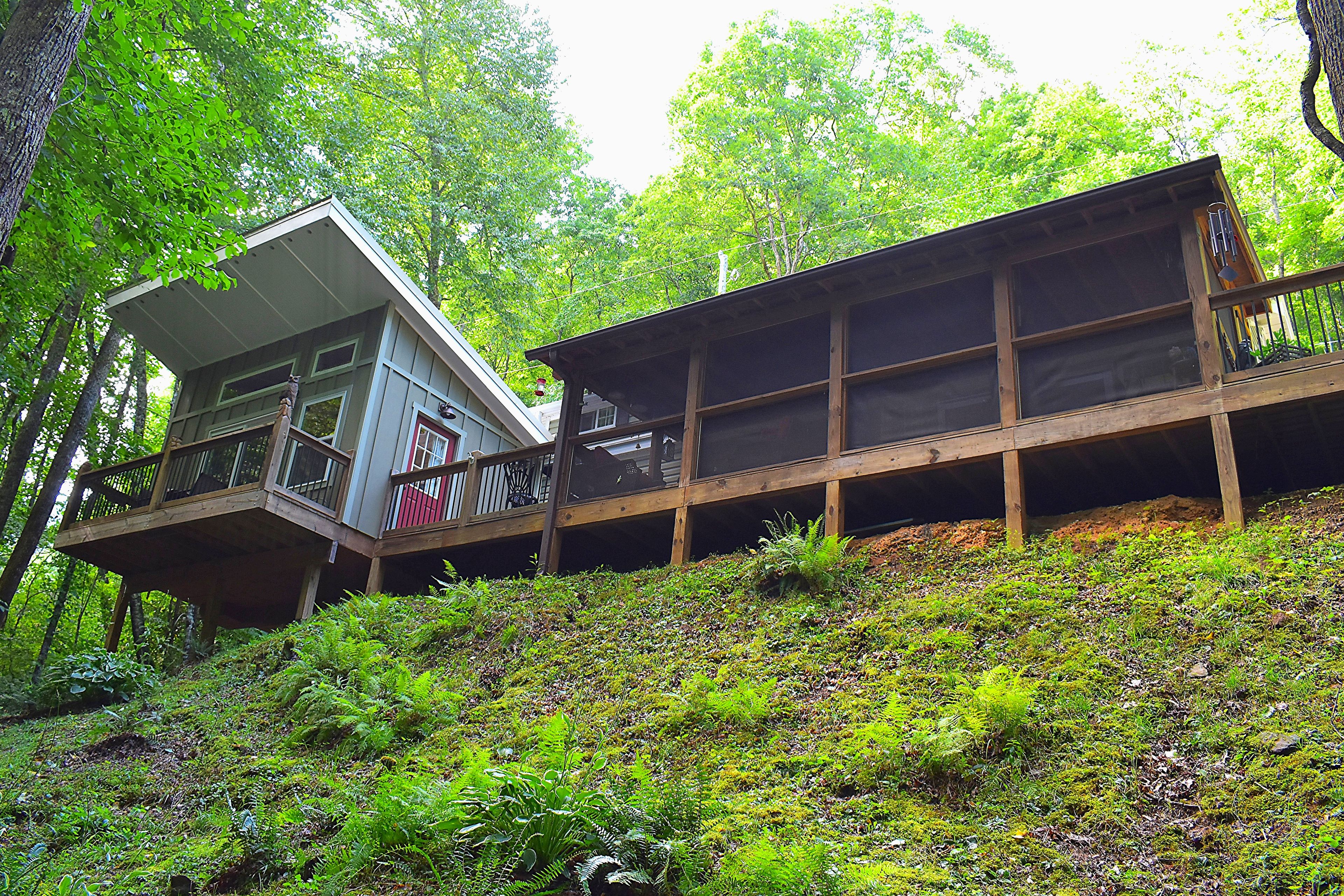Una cabaña con balcón y terraza, rodeada de bosque denso.