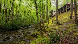 A forested area with a stream, a wooden building with a balcony, and an American flag. - The Owl's Perch (5 inch clearance needed) (Robbinsville)