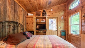 A wooden cabin bedroom with a plaid bedspread, a television, and a small window. - The Owl's Perch (5 inch clearance needed) (Robbinsville)
