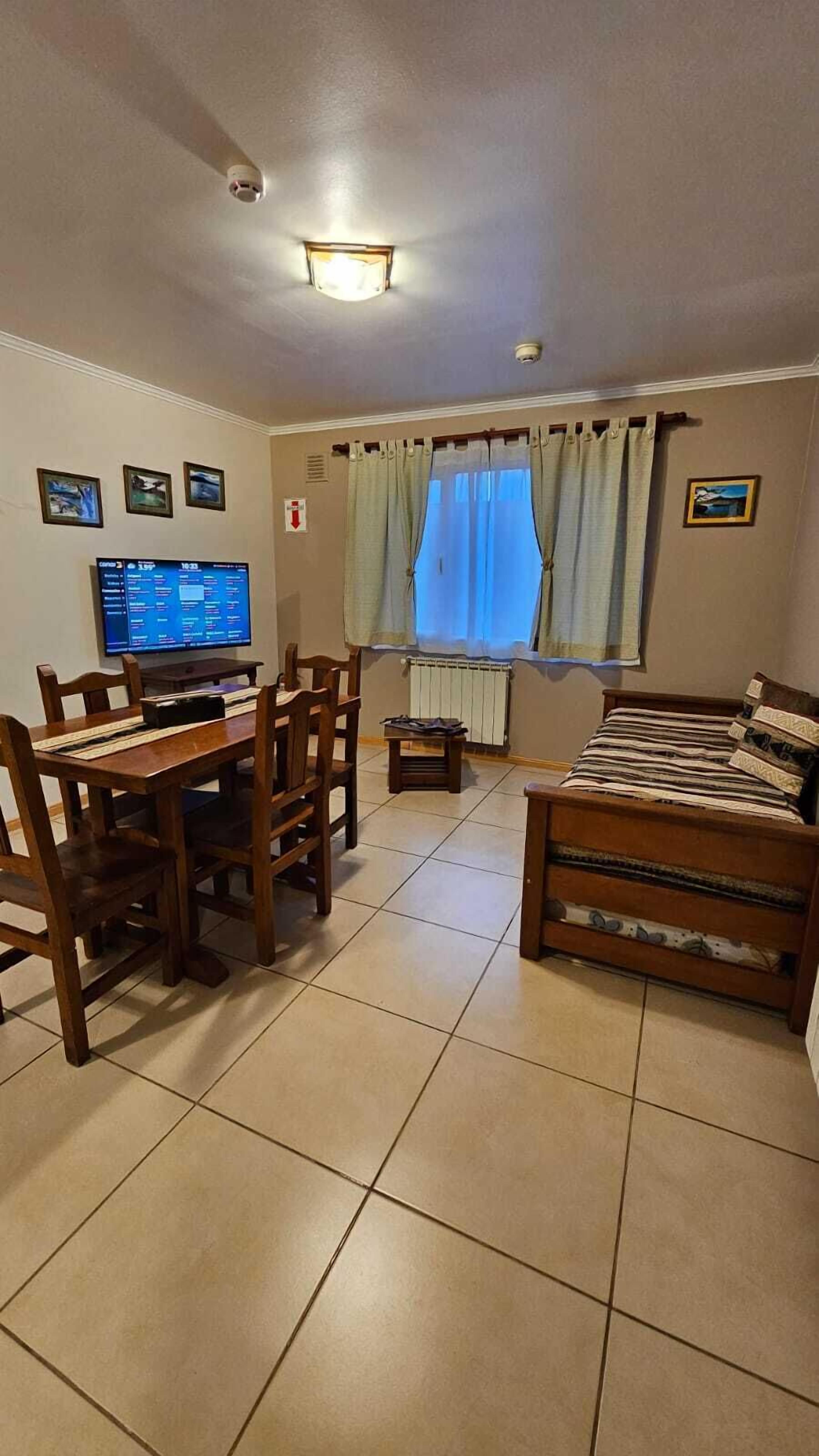 A living room with a dining table, chairs, a sofa, a TV, and a window with curtains.