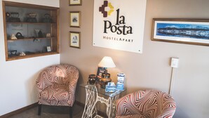 Ein gemütlicher Winkel mit zwei gemusterten Sesseln, einem Glastisch und einer Lampe, sowie einem gerahmten Schild für 'la Posta Hostel Apart'.