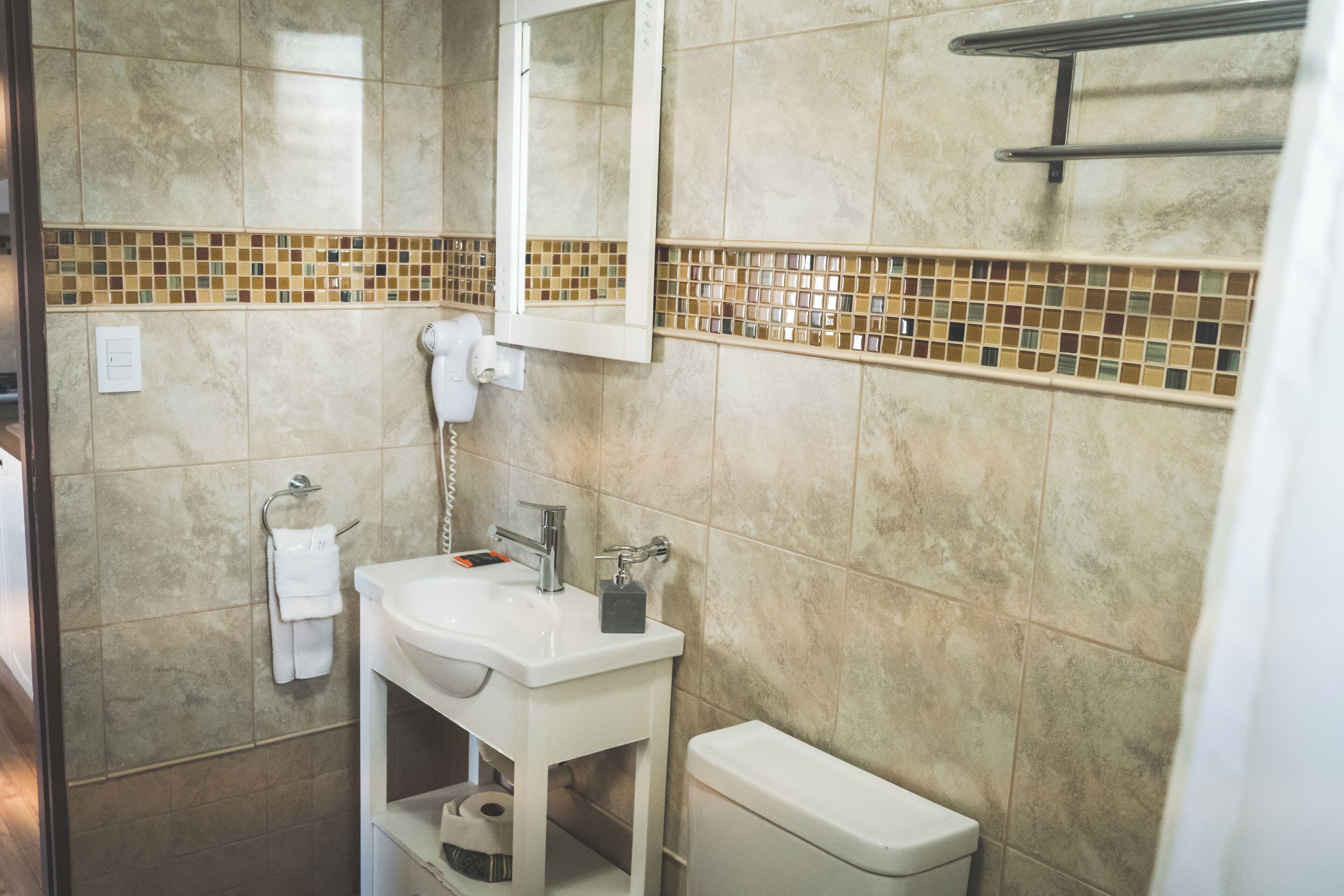 A bathroom with a white sink, mirror, and toilet. There is a towel rack and a shower head on the wall.