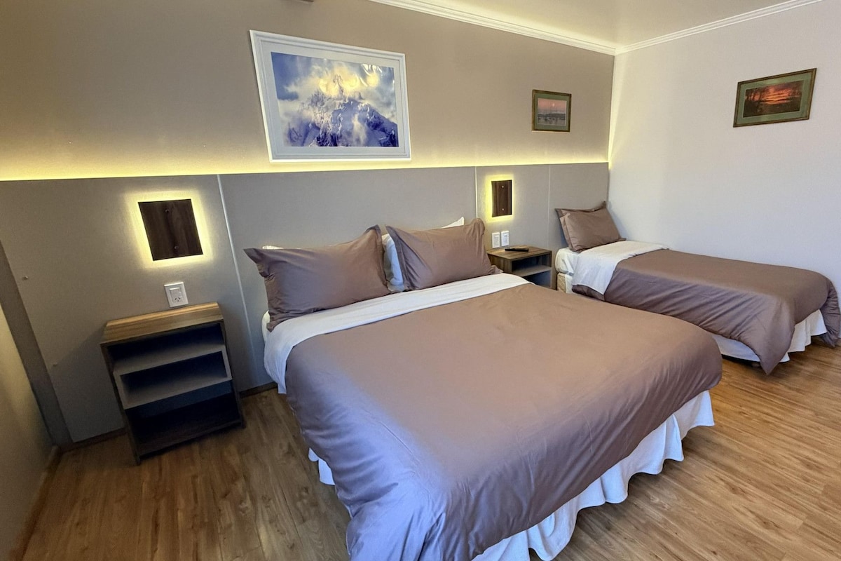 Habitación de hotel con dos camas, una mesita de noche, una lámpara de pared y un cuadro enmarcado sobre las camas.