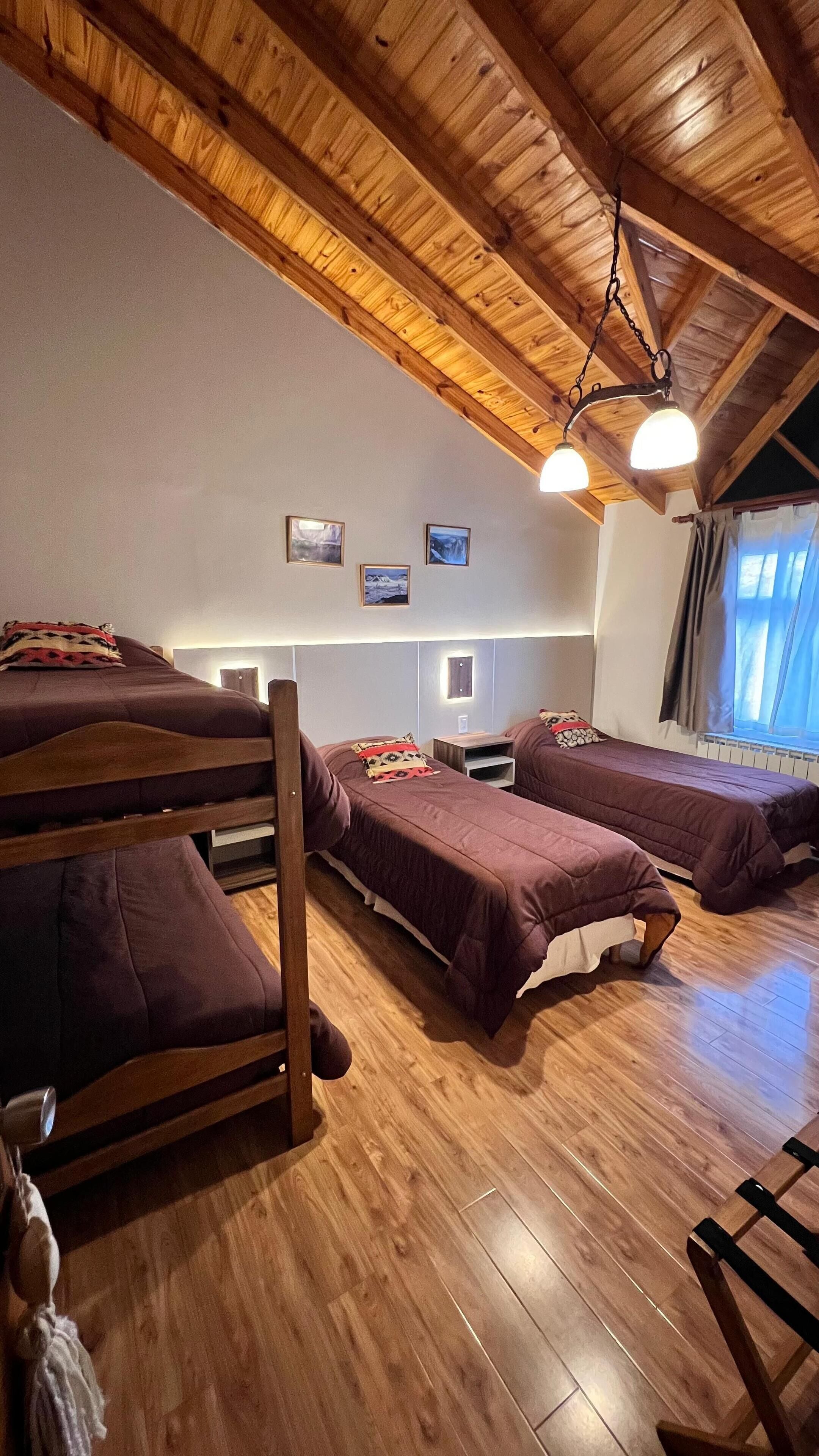 A room with wooden floors, bunk beds, a hanging light fixture, and framed pictures on the wall.