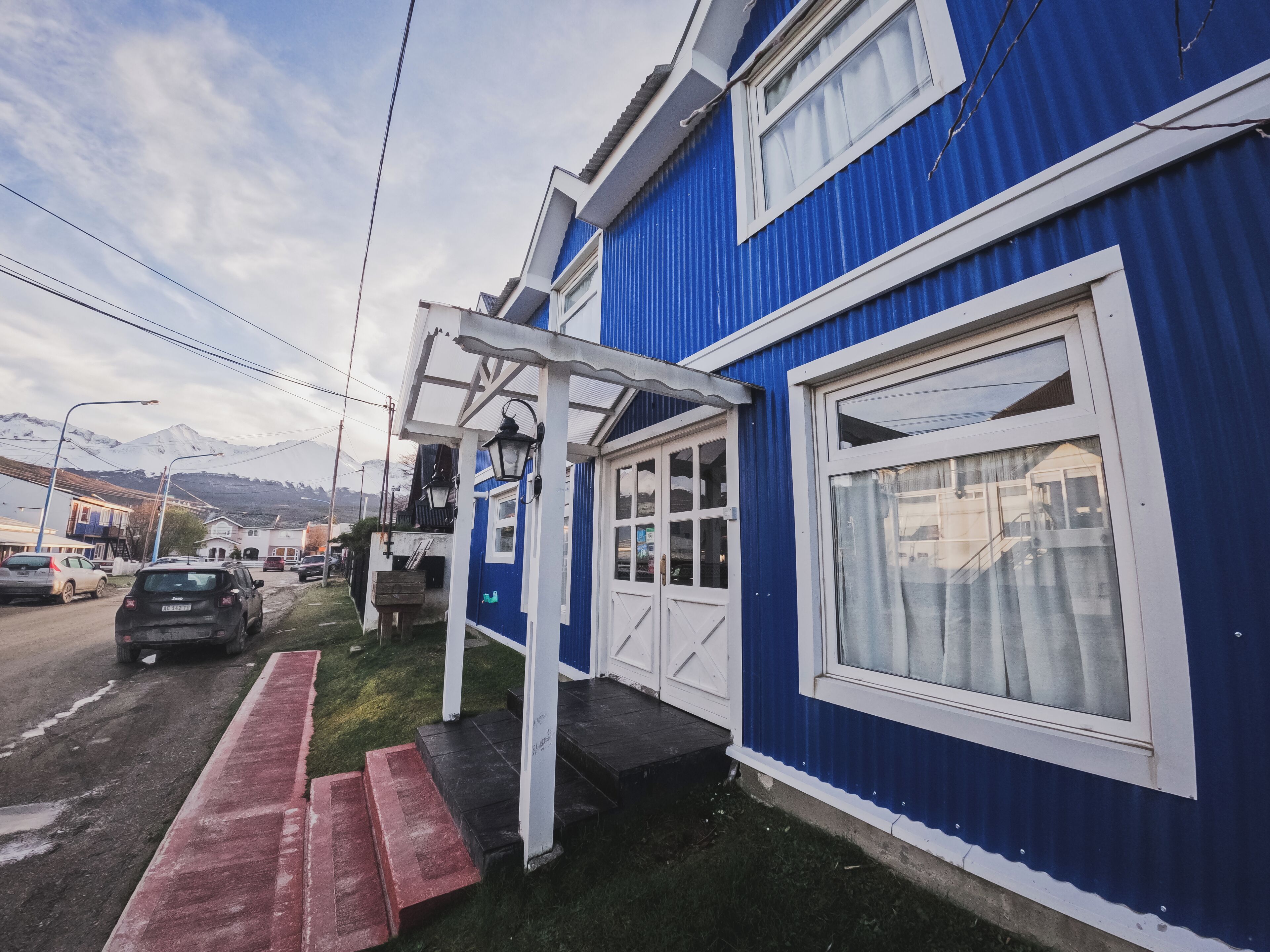 A blue building with a white door and windows, a porch, and a red pathway leading to the entrance.
