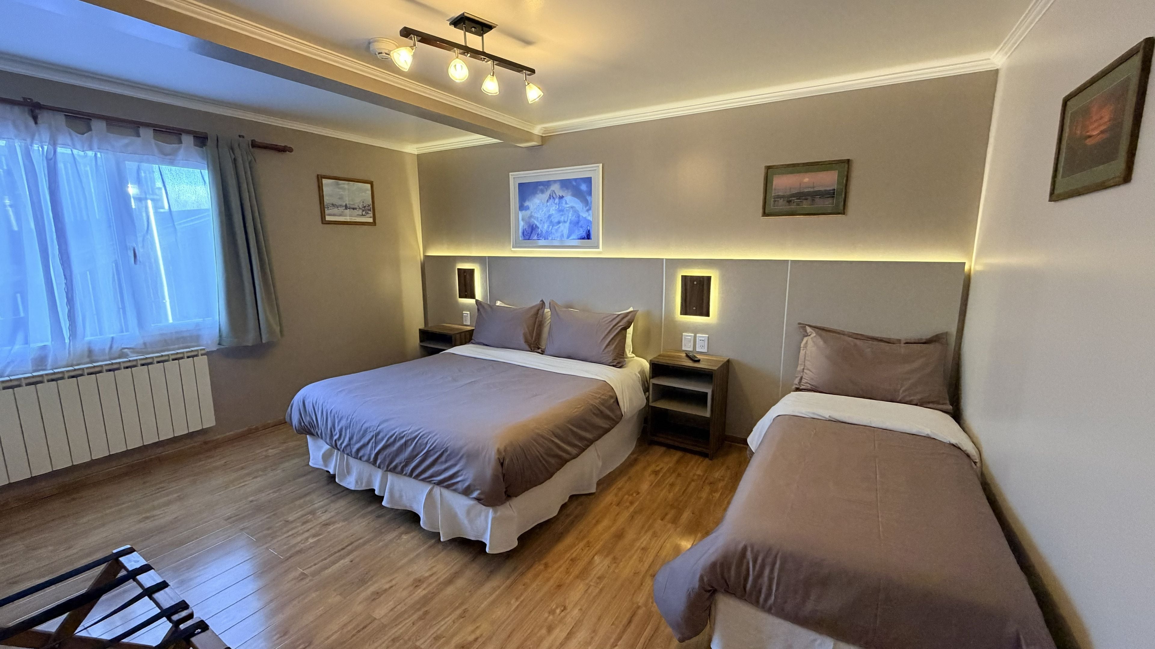 Habitación de hotel con dos camas, una ventana con cortinas, un radiador y luces en la pared.