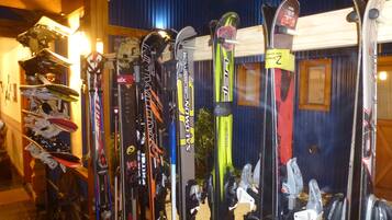 Una colección de esquíes y tablas de snowboard en una habitación de madera con pared azul y una ventana.