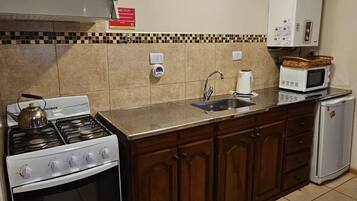 A kitchen with a gas stove, oven, microwave, and a small refrigerator.