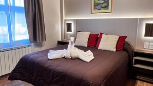 A bedroom with a wooden ceiling, a large bed with a brown duvet, red and white pillows, and a towel art piece. There is a painting on the wall and a window with curtains. - La Posta Apart (Ushuaia)