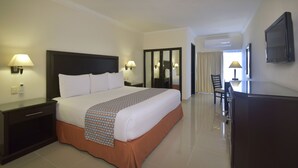 A hotel room with a large bed, bedside lamps, a desk with a chair, a TV, and a wardrobe. - Hotel Bonampak (Cancun)
