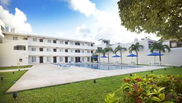 Un hotel con piscina, mobiliario exterior y palmeras.
