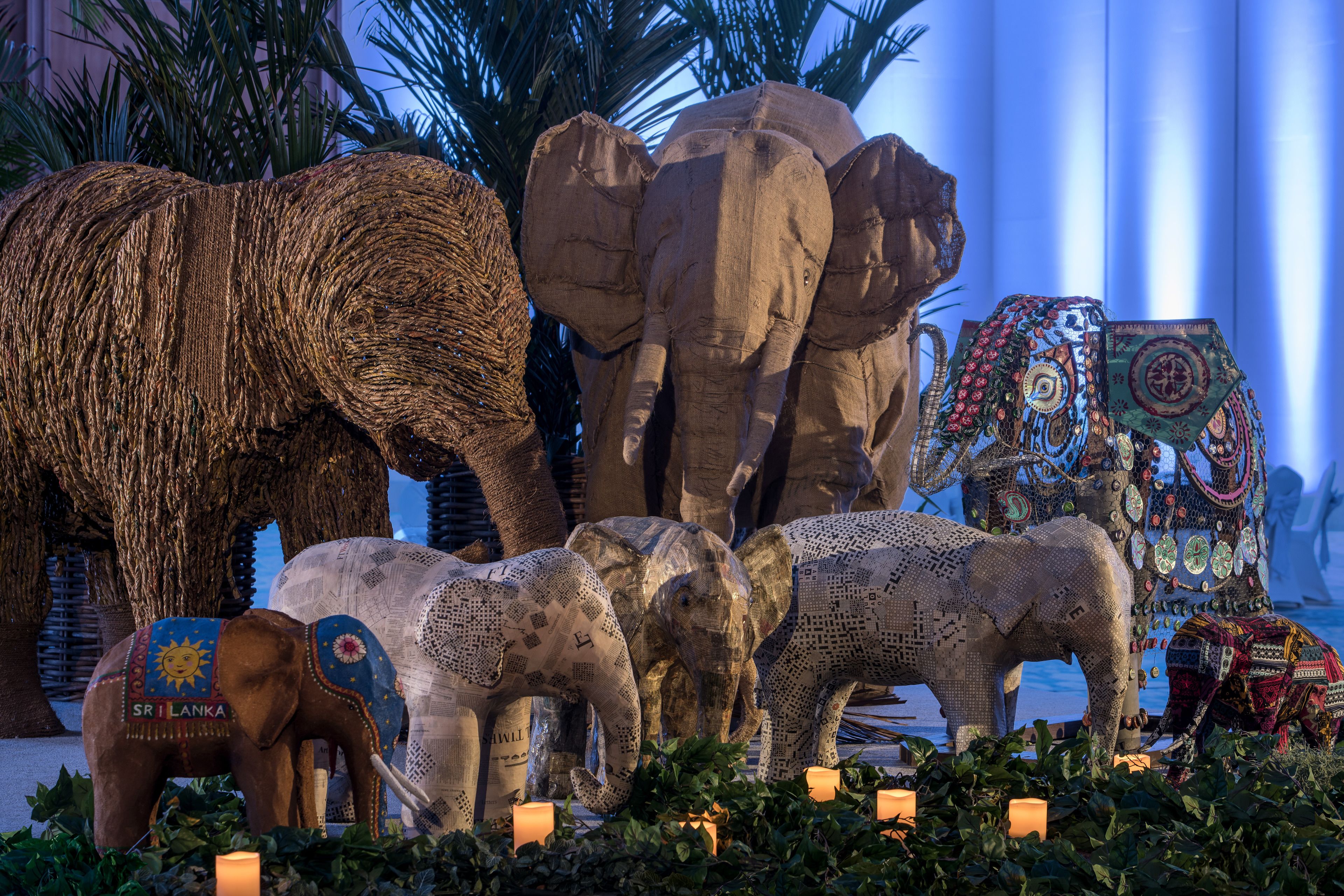 A display of elephants with intricate patterns and designs, surrounded by greenery and candles.