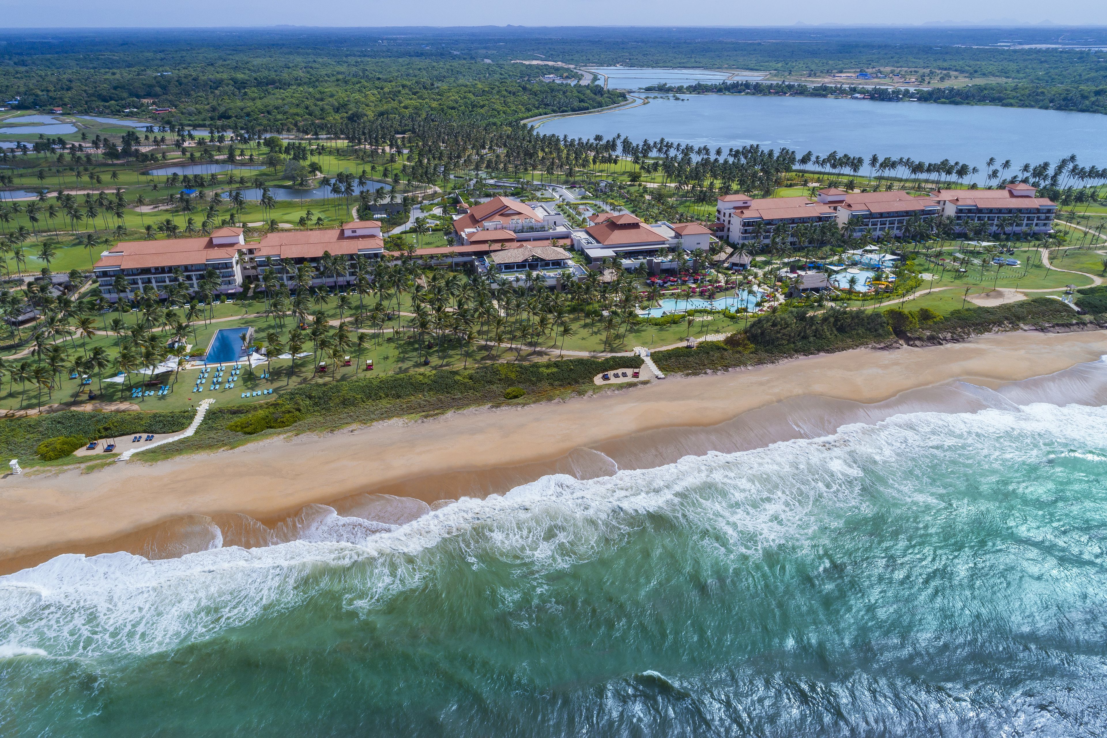 Luftaufnahme eines Resorts mit mehreren Gebäuden, einem Strand und einem Gewässer.
