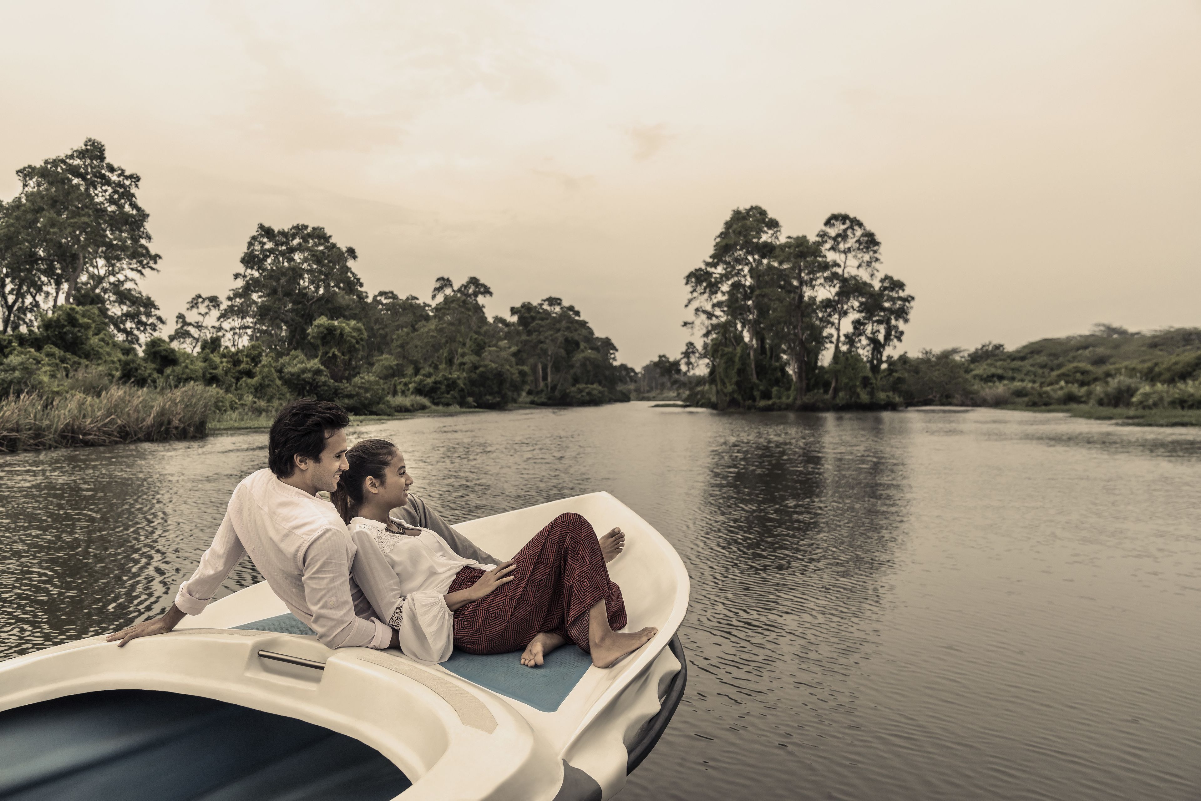 A boat with two people sitting on the edge, surrounded by calm water and greenery.