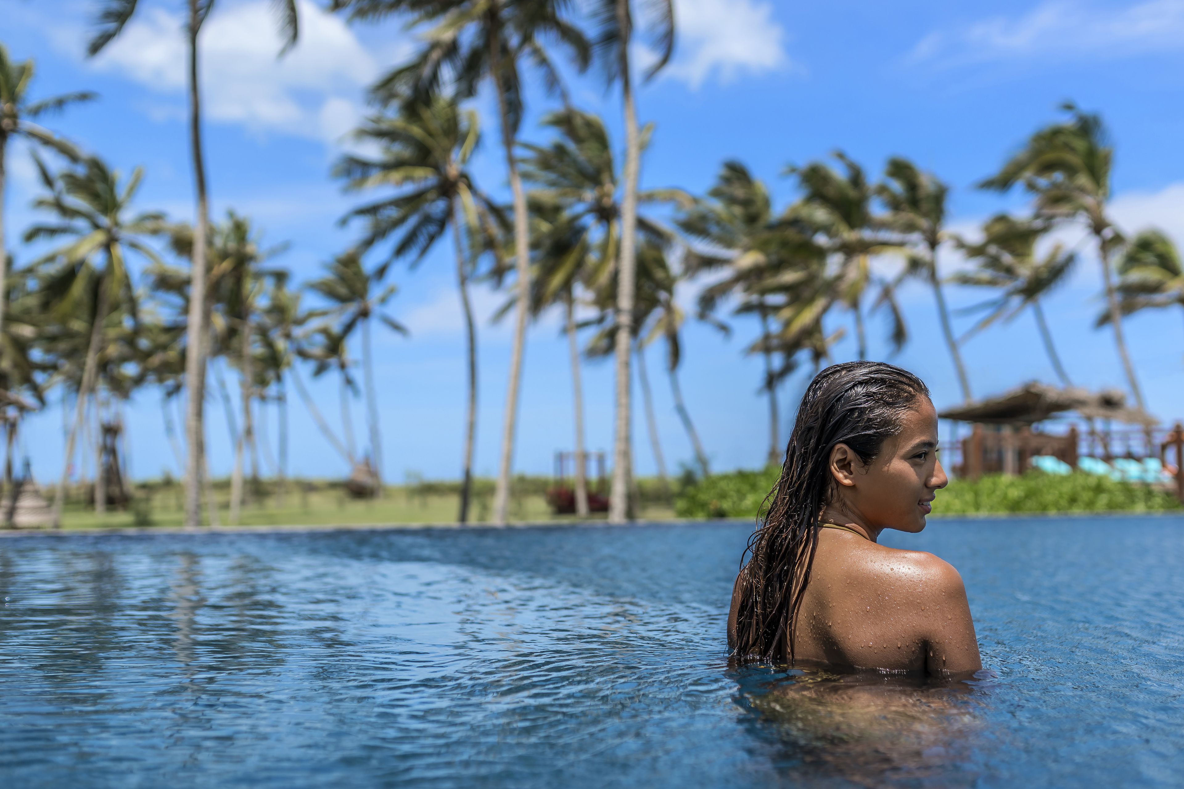 A person in a clear blue pool with palm trees in the background.