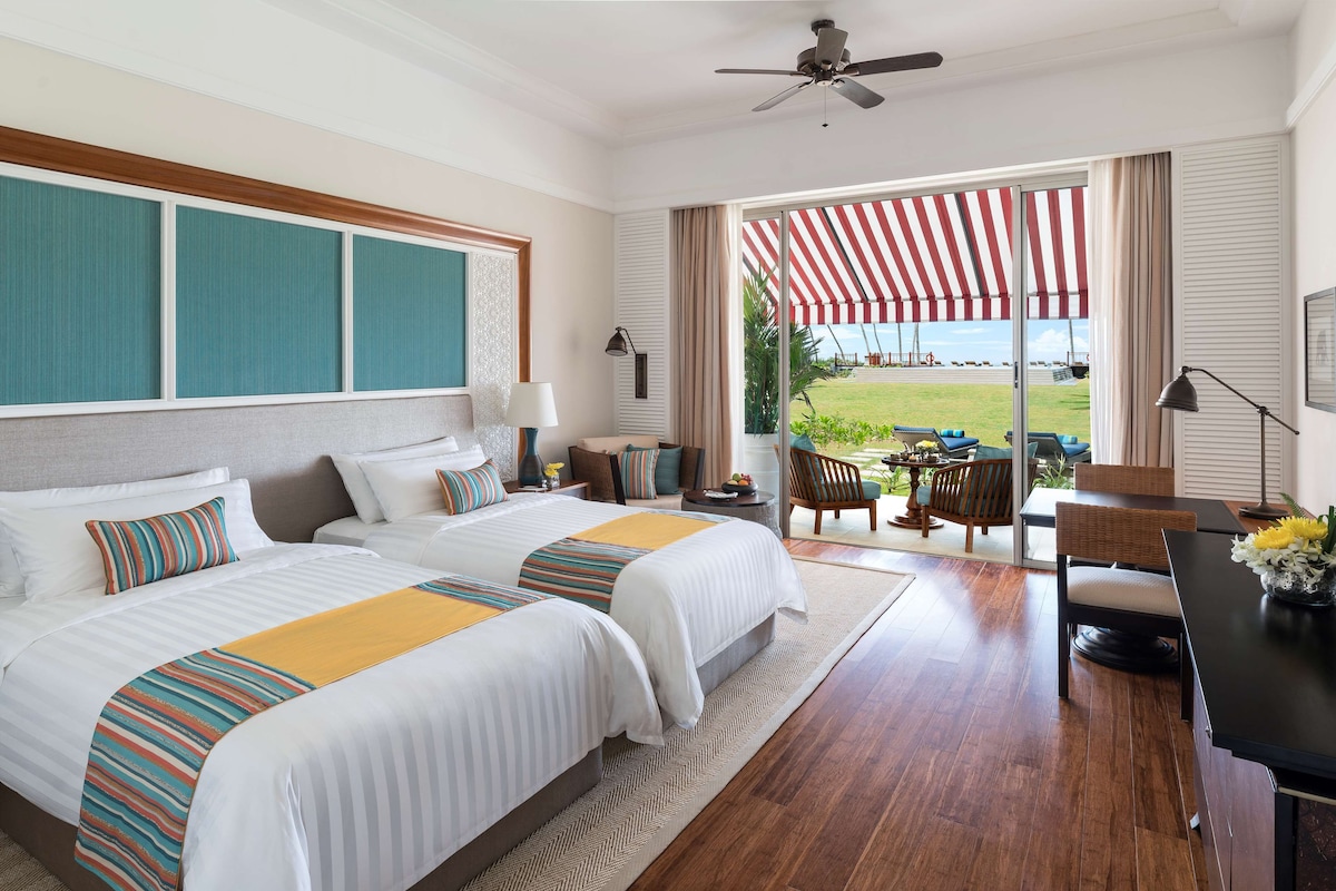 Une chambre d’hôtel avec deux lits, un bureau et vue sur la plage.