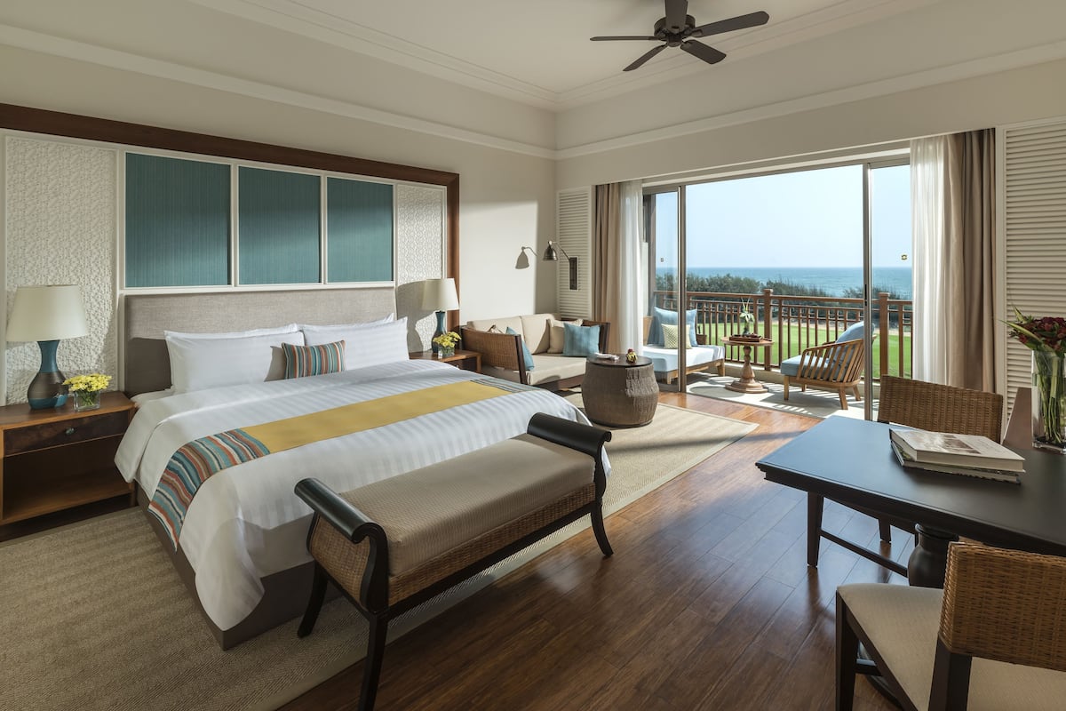Een hotelkamer met een groot bed, een eettafel en een balkon met uitzicht op de oceaan.